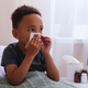 A boy holding a tissue blowing his nose in bed with cold symptoms