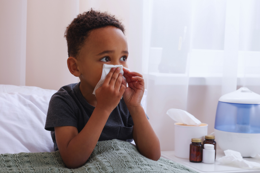 A boy holding a tissue blowing his nose in bed with cold symptoms