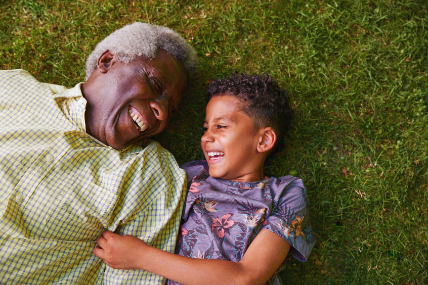 Grandfather and young grandson lying on the grass and laughing together