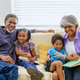 Grandparents sitting with their two grandchildren on a couch at home, looking at books together