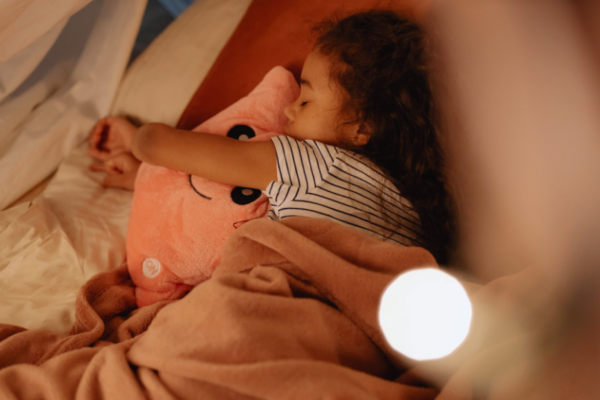 A young girl embracing a pink plush toy while sleeping comfortably in her cozy bed