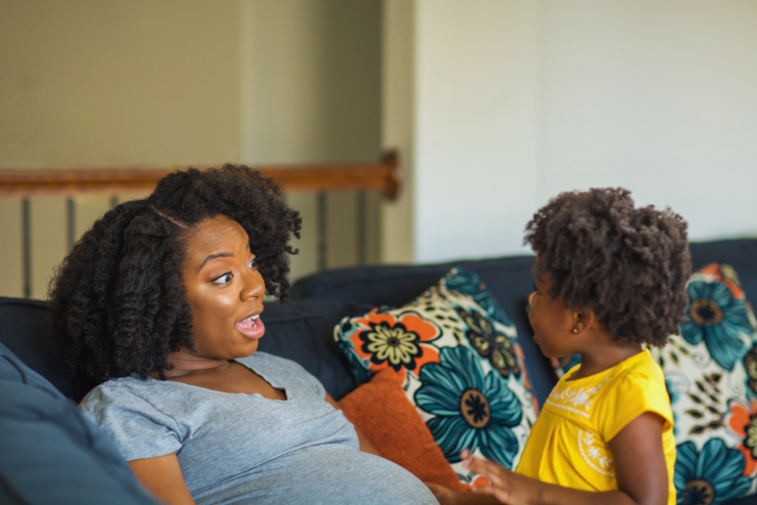 Pregnant mother talking with her daughter while in the couch at home