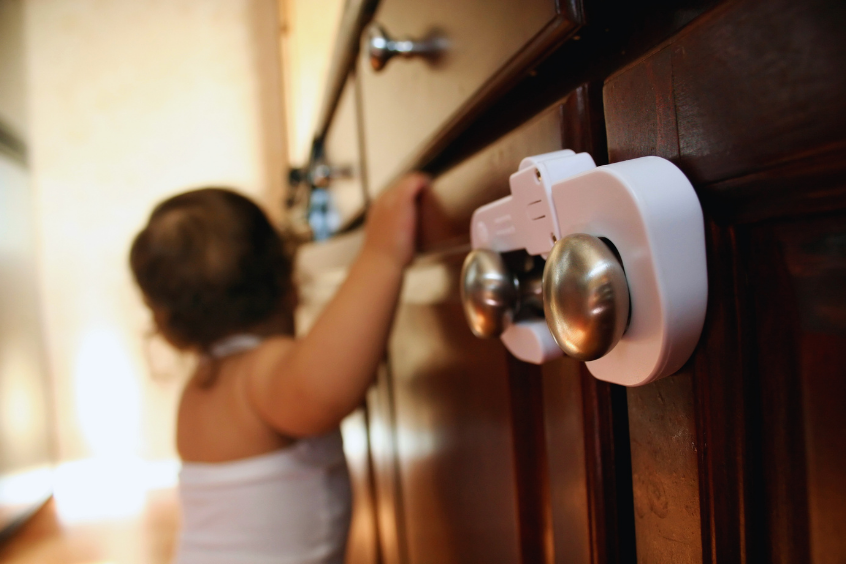 Baby reaching toward a cabinet with a child safety lock